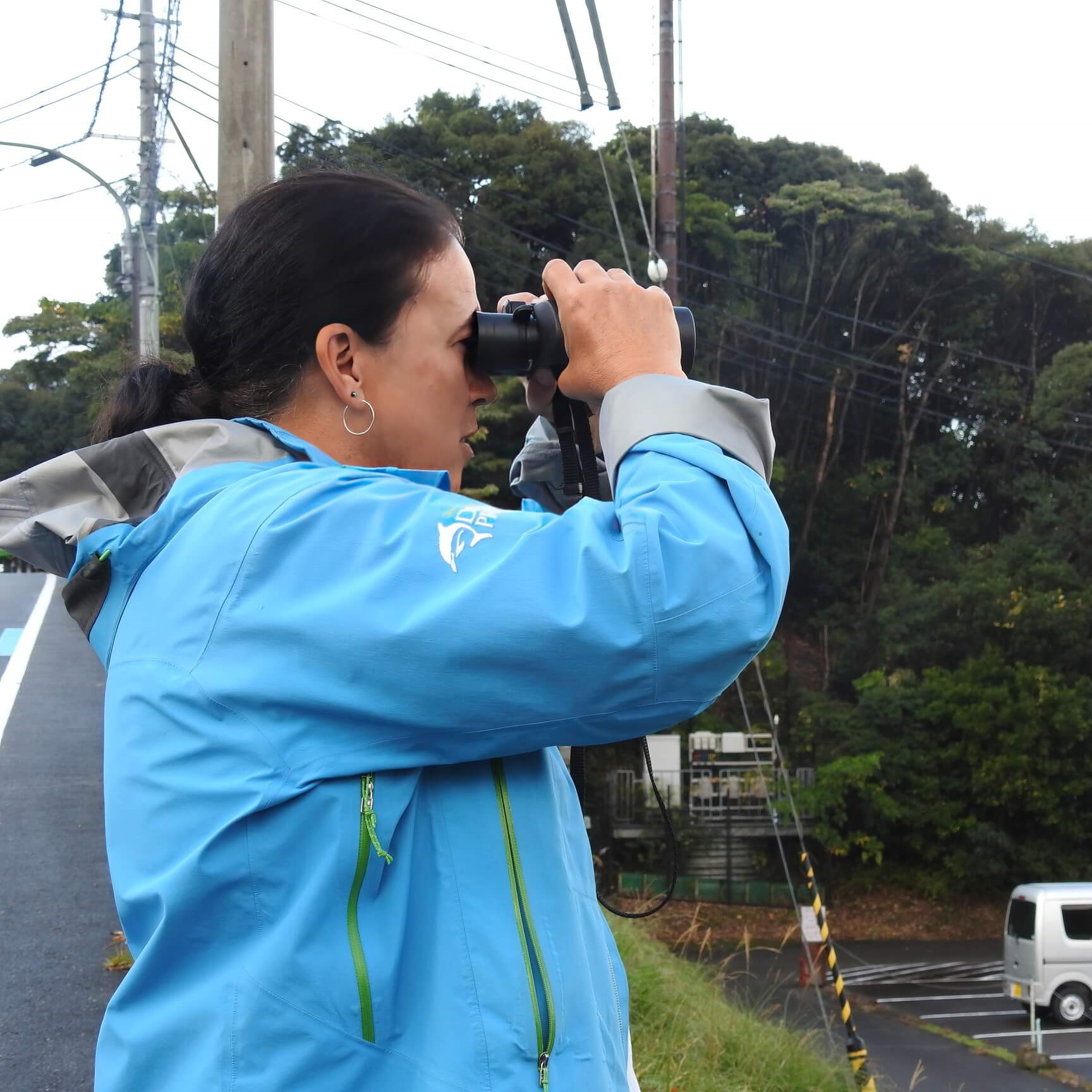 Cynthia with binoculars watching dolphin capture in Taiiji, Japan