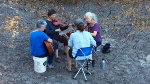 Sharry and 3 friends sitting knee-to-knee playing musical instruments in the outdoors